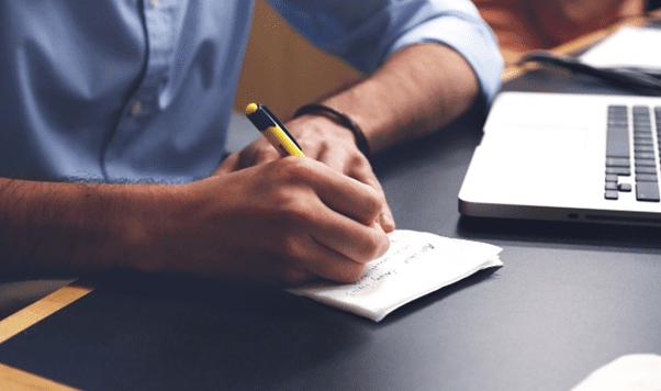 man writing notes with pen and paper